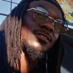 A headshot of an artist with dreads and sunglasses